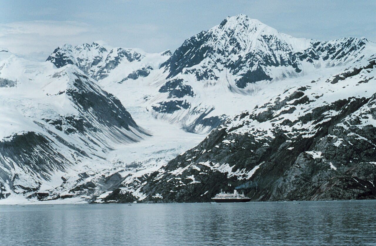 A small cruise ship dwarfed by towering ice cliffs in Glacier Bay, Alaska
